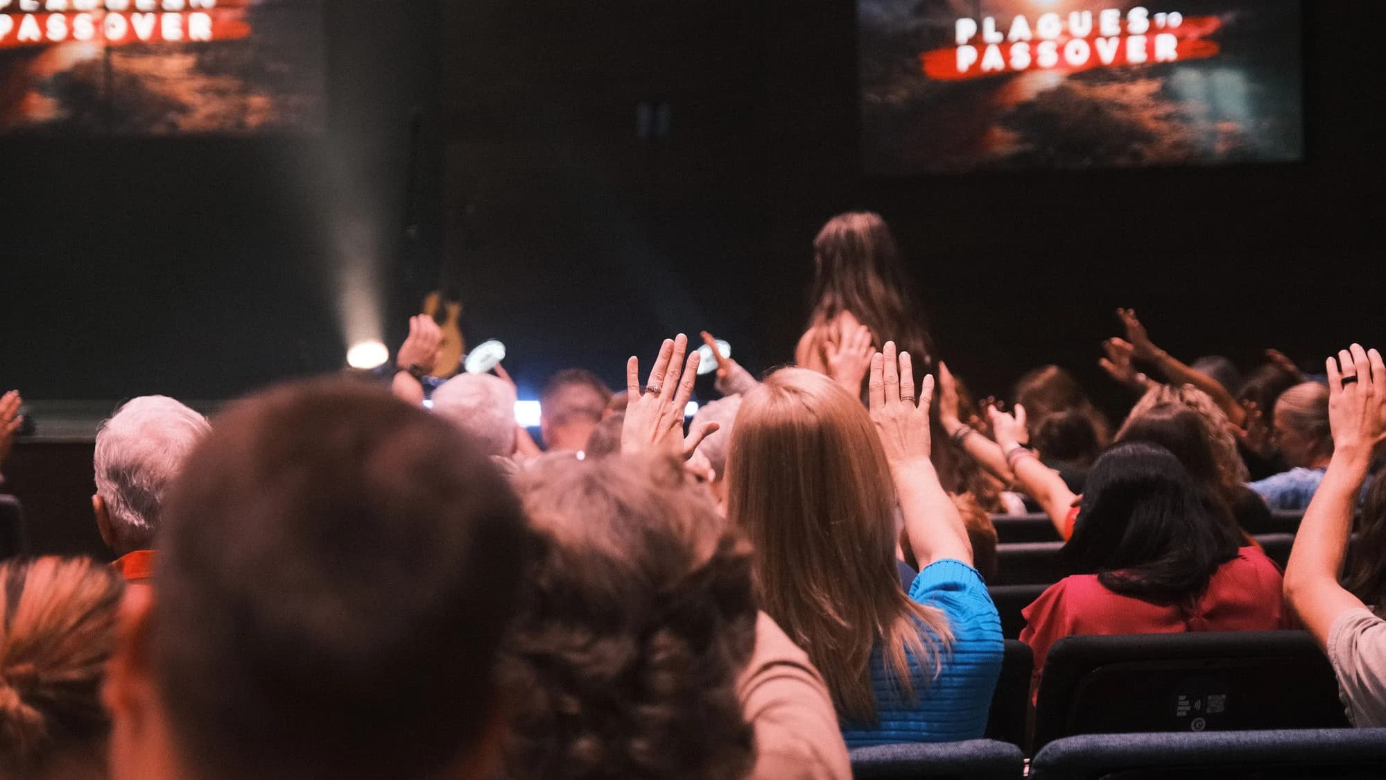 Hands raised across the room in prayer during a Discovery Church worship gathering.
