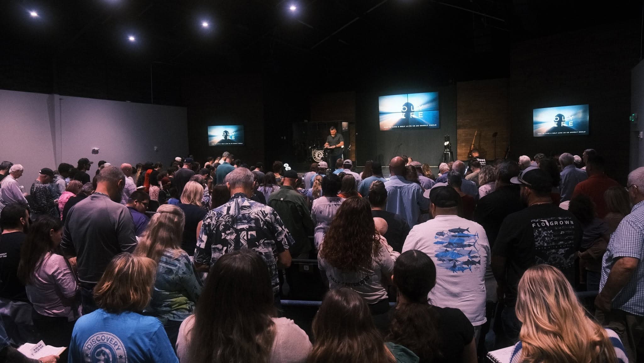 Discovery Church gathered in worship on a Sunday morning, hands raised under stage lights.