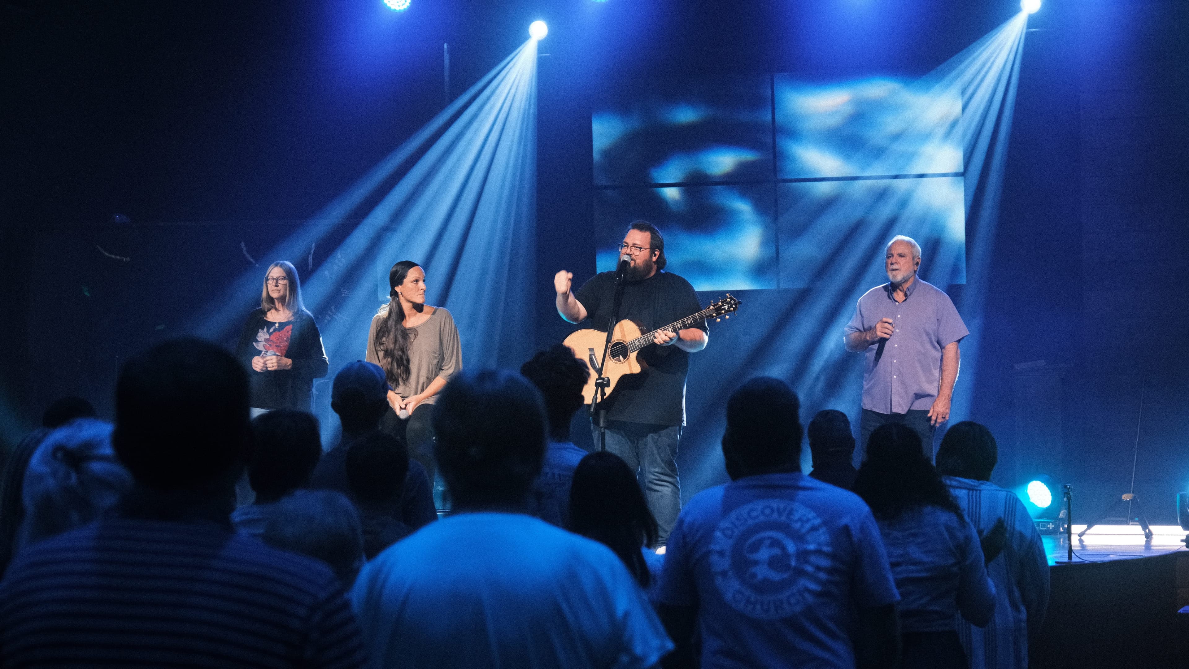 A Sunday worship gathering at Discovery Church, hands raised.